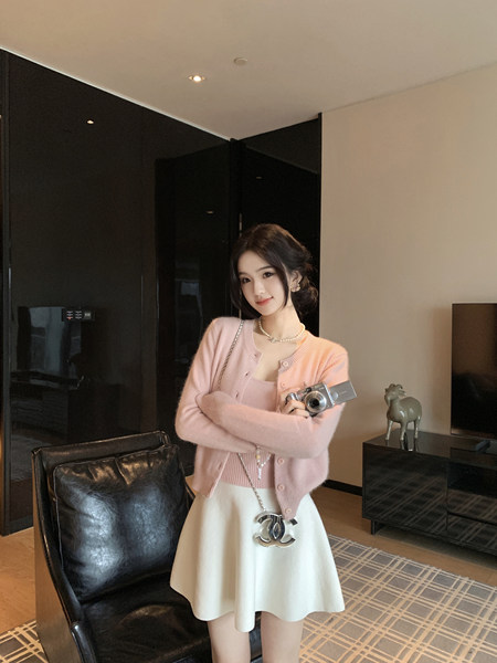 Woman wearing a pink cardigan and white skirt, holding a camera.