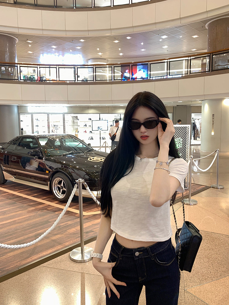 Woman wearing white crop top and dark jeans in a mall setting with a classic car in the background
