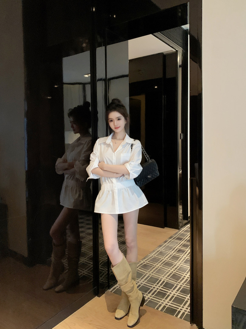 Woman wearing white shirt dress and tan knee-high boots, posing in front of mirror