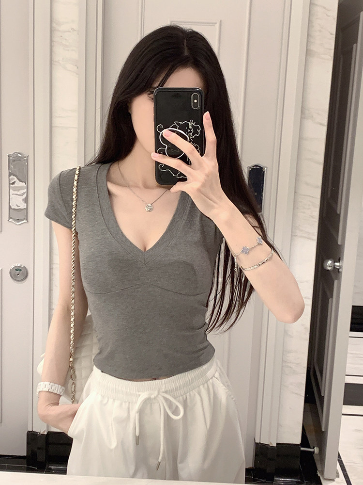 Woman taking mirror selfie wearing gray V-neck top and white drawstring pants