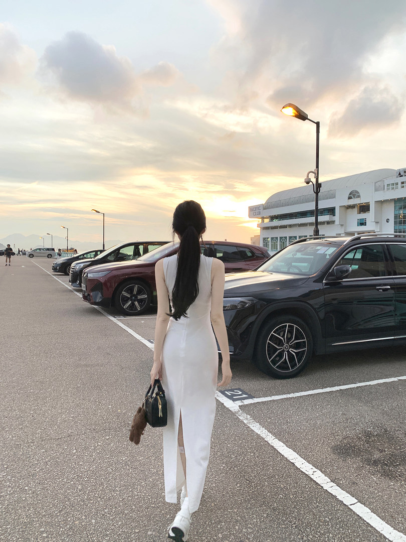 Woman wearing a white sleeveless dress walking in a parking lot at sunset