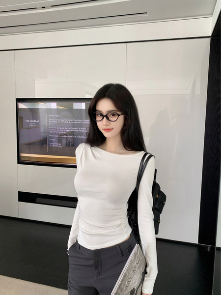Woman wearing a white long-sleeve top and gray pants, carrying a black bag and holding a magazine.