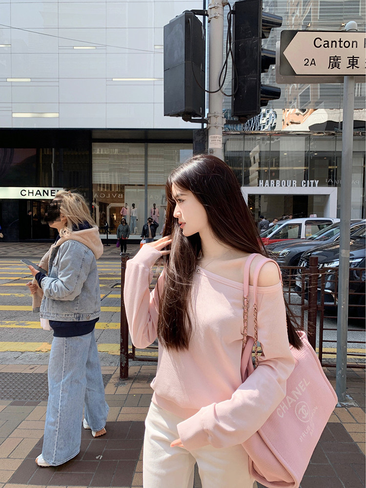 Woman wearing pink off-shoulder top and white pants on city street, carrying pink Chanel bag