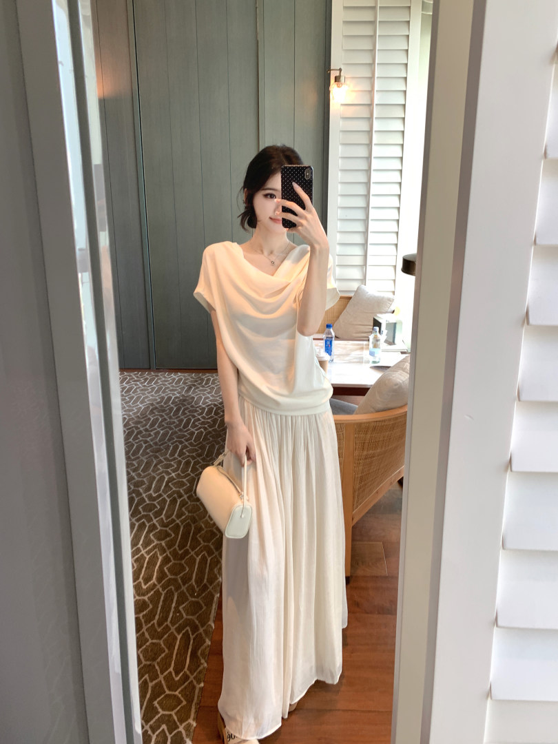 Woman taking mirror selfie wearing white draped top and long skirt