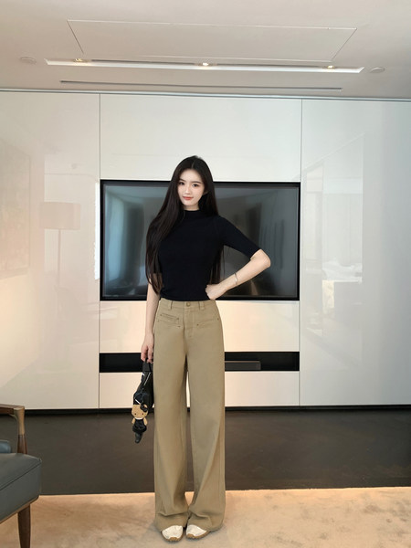 Woman wearing black short-sleeve top and beige wide-leg pants, holding a small bag with a plush keychain.
