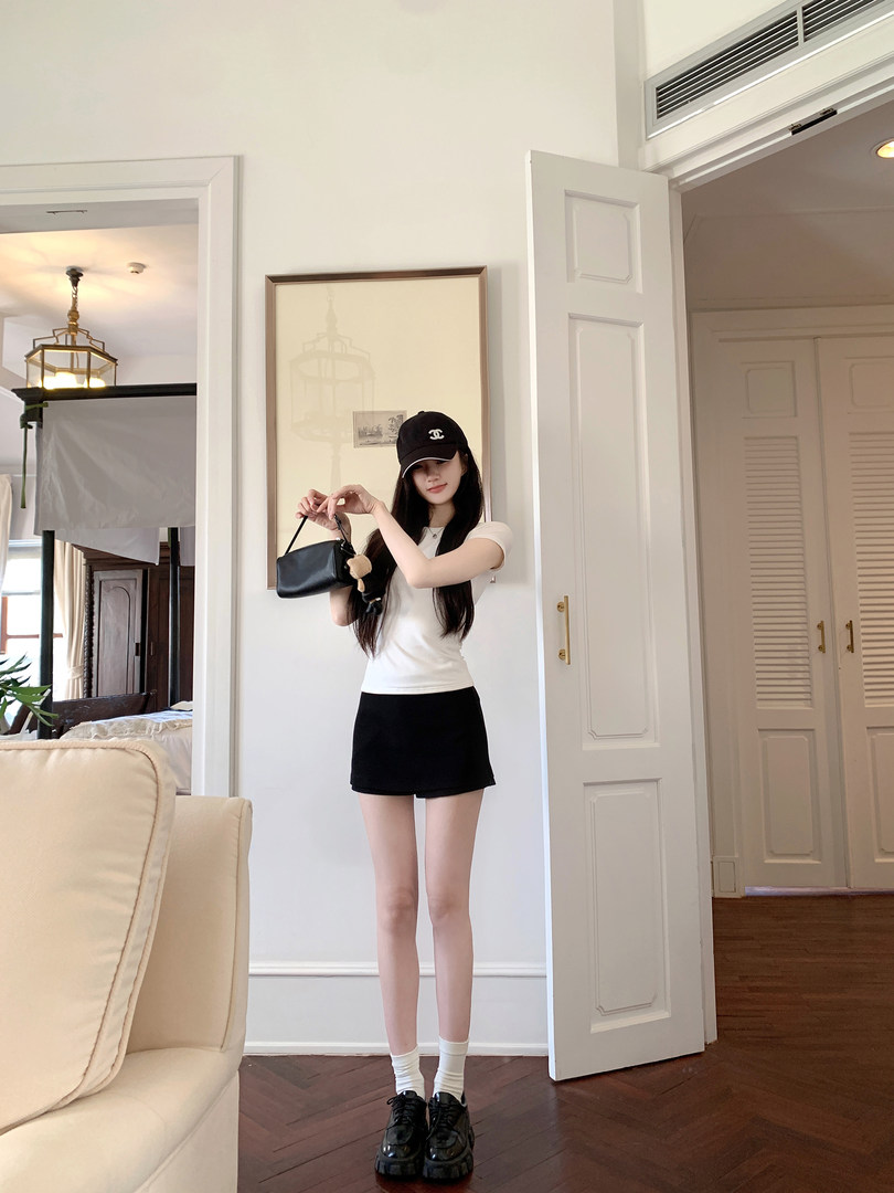 Woman wearing white t-shirt, black shorts, and holding a black handbag indoors