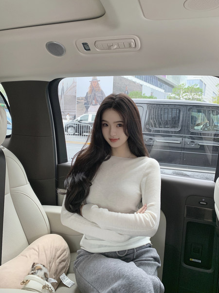 Woman wearing a white long-sleeve top and gray sweatpants sitting in a car