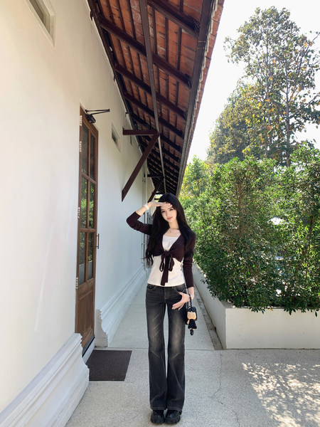Woman wearing a white top with a brown cardigan tied at the front, paired with dark flared jeans and black platform shoes, standing outdoors.