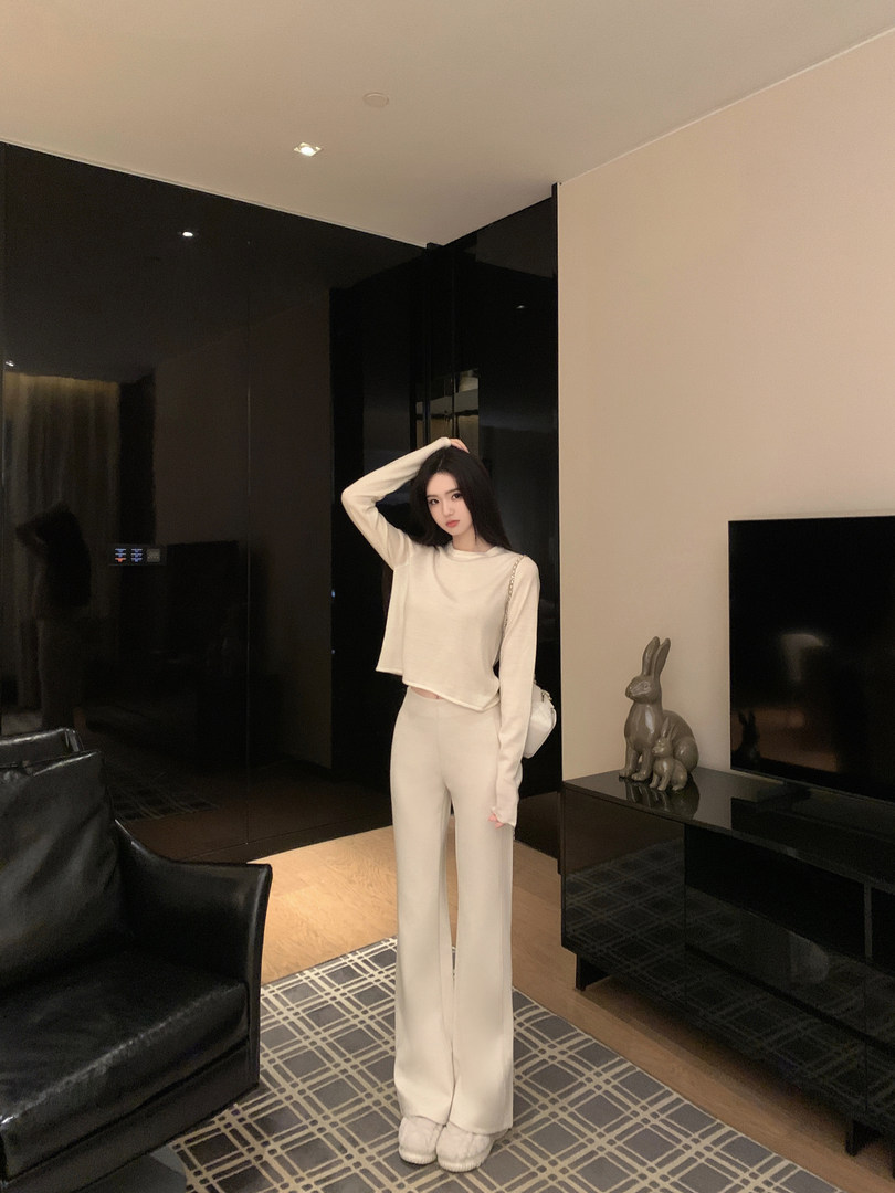 Woman wearing a white long-sleeve crop top and matching wide-leg pants in a modern living room.
