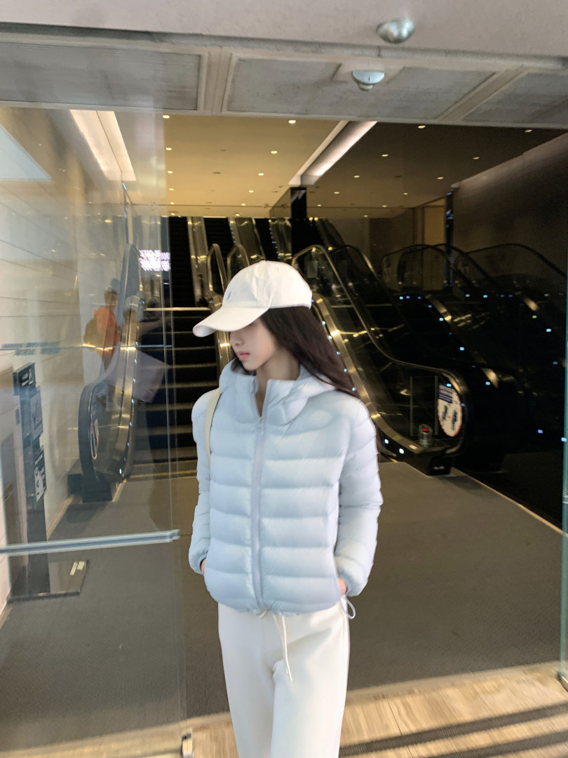 Woman wearing a light blue puffer jacket and white pants in a mall setting