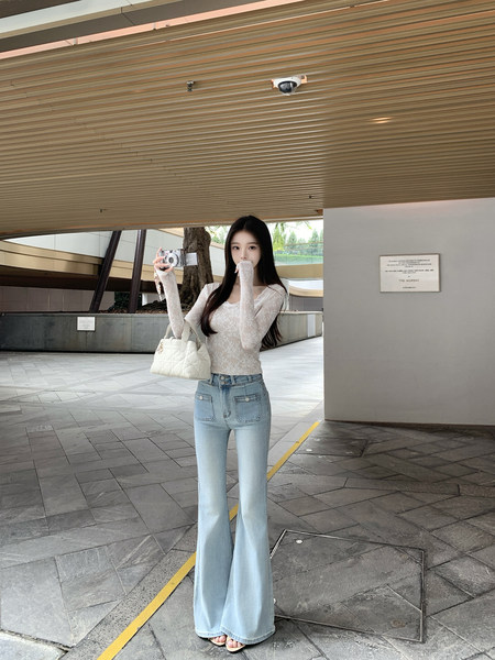 Woman wearing lace top and light blue flared jeans, holding camera and white quilted bag