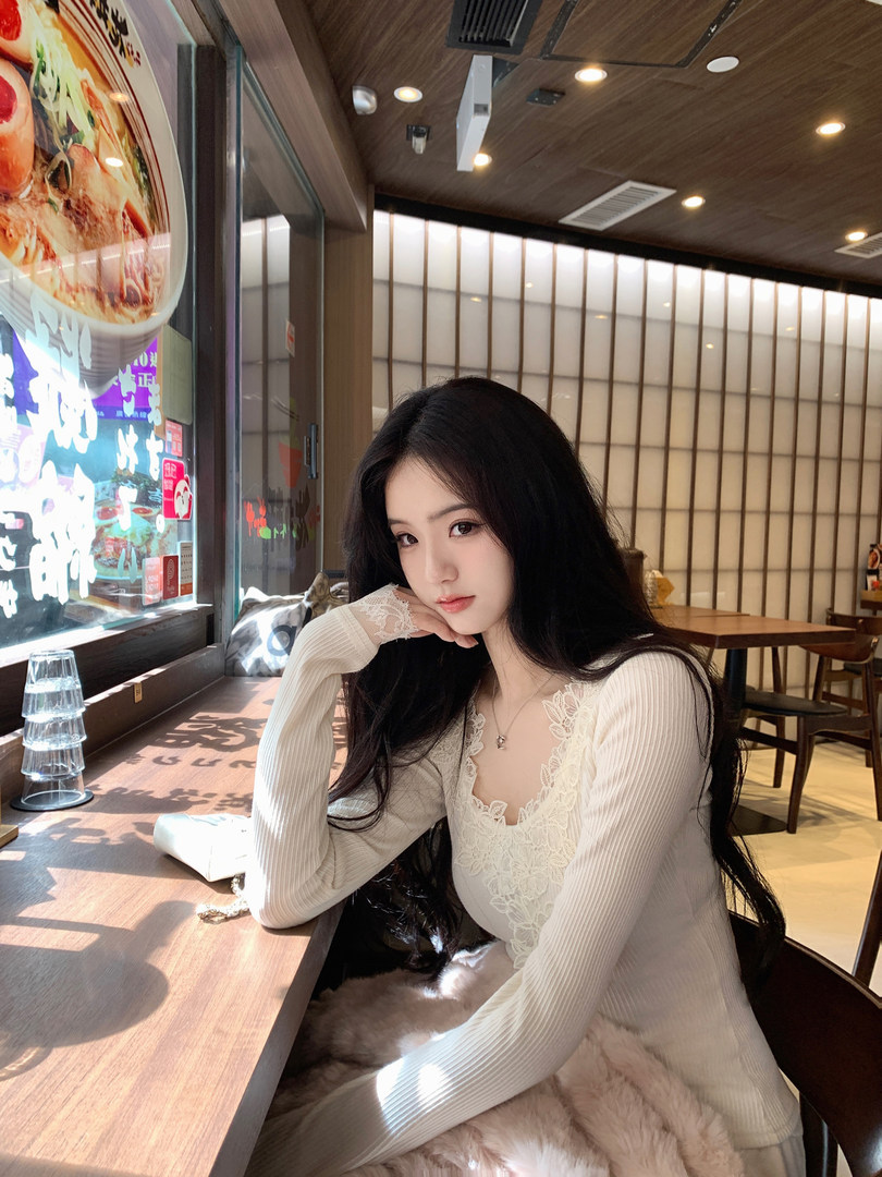 Woman wearing a cream-colored ribbed long-sleeve top with lace detailing, seated in a restaurant