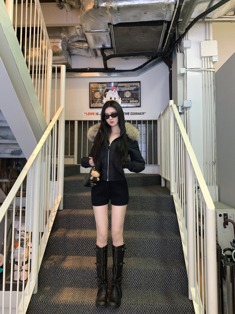 Woman wearing black puffer jacket with fur hood, black shorts, and black boots standing on stairs