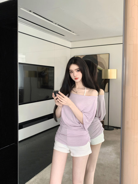 Woman wearing a lavender off-shoulder top and white shorts, taking a mirror selfie.