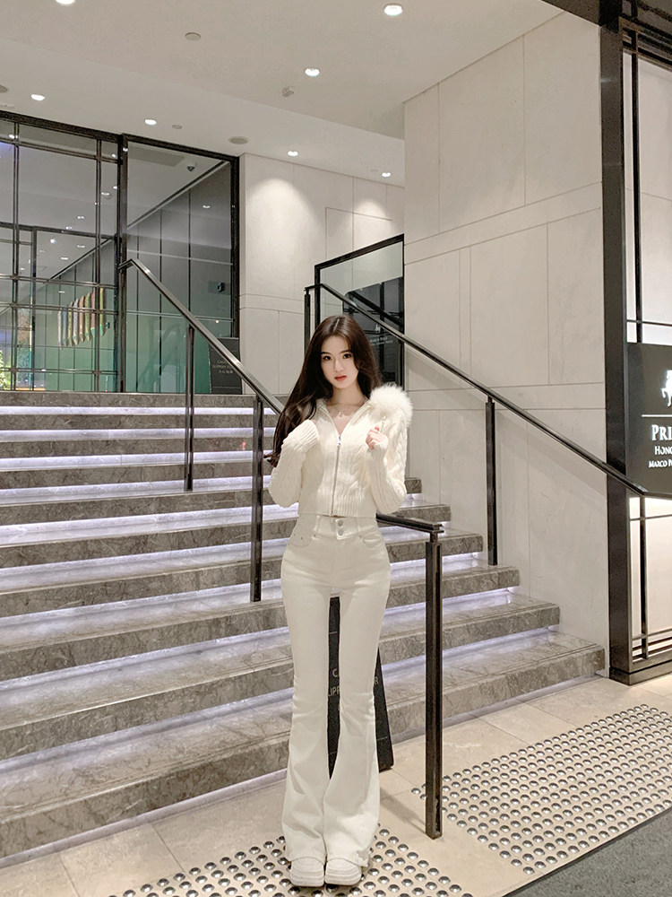 Woman wearing a white knit sweater with fur trim and matching white pants, standing on stairs.