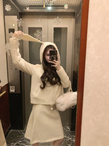 Woman taking mirror selfie wearing a cream-colored hooded knit sweater and matching skirt with a fluffy bag.