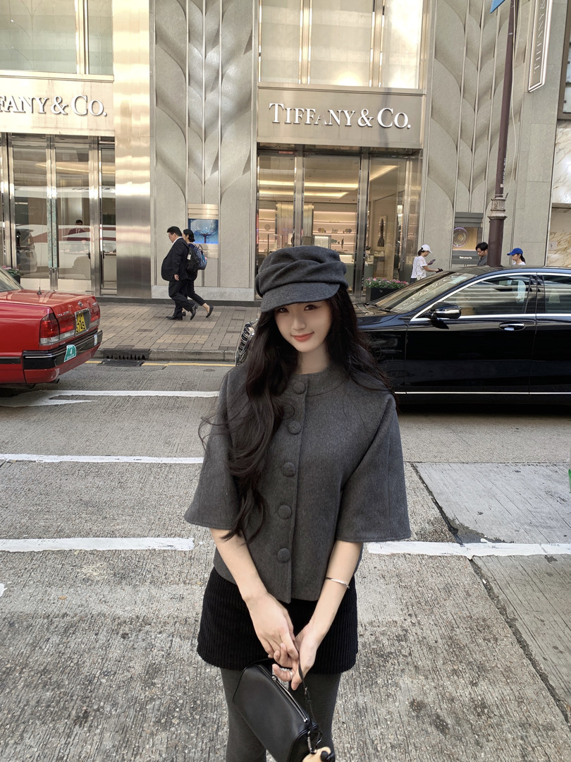 Woman wearing a gray coat and matching hat, standing on a city street with a Tiffany & Co. store in the background.