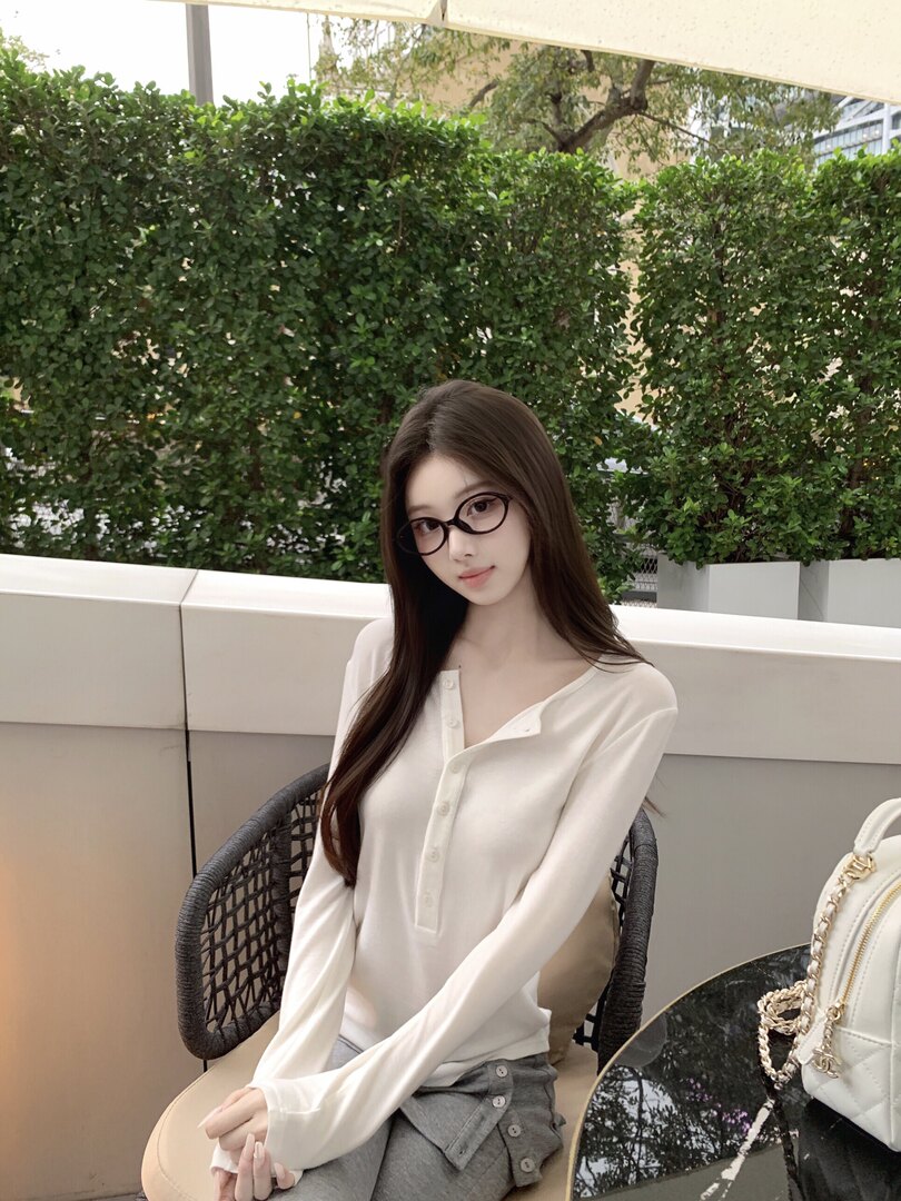 Woman wearing a white long-sleeve button-up top and gray pants, seated outdoors.