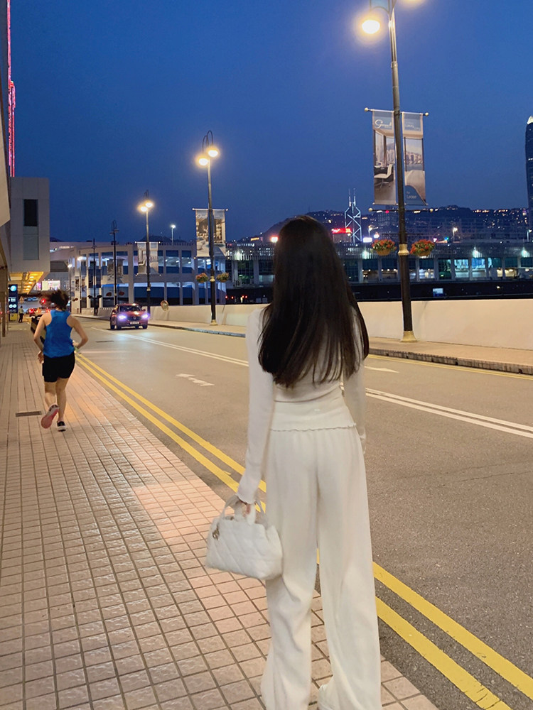 Woman wearing white outfit walking on city street at dusk