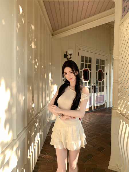 Woman wearing a cream-colored ribbed dress with ruffled hem standing in a sunlit corridor.