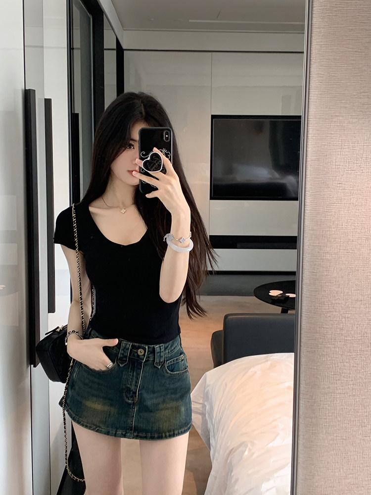 Woman taking mirror selfie wearing black top and denim skirt