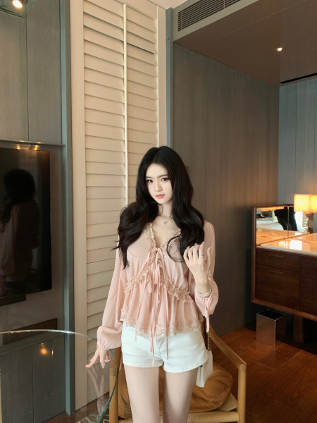Woman wearing a pink lace-trimmed blouse and white shorts in a modern room setting