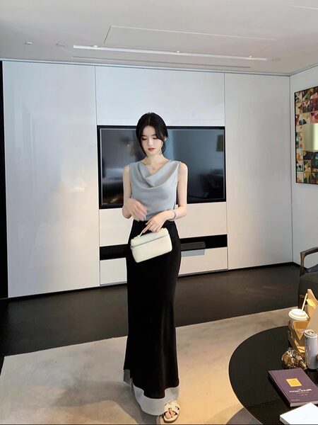 Woman wearing a sleeveless gray top and black skirt, holding a white handbag.