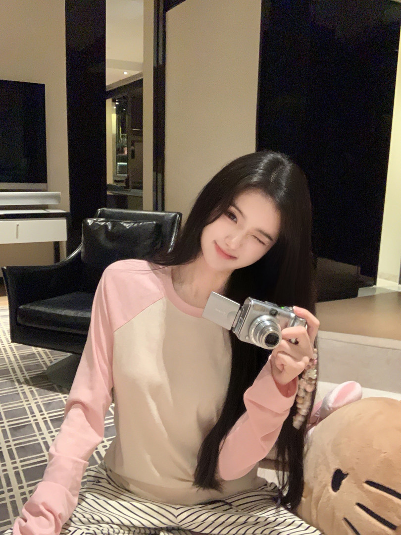 Woman wearing a pink and beige long-sleeve top while holding a camera