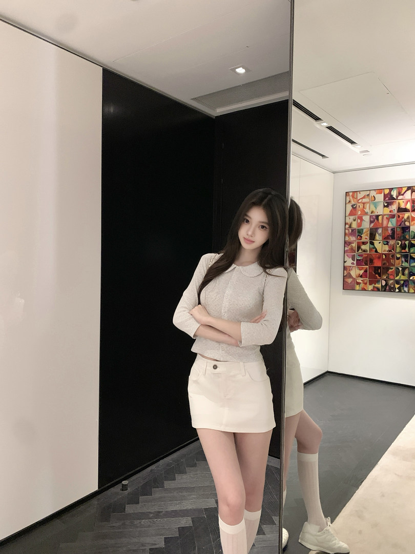 Woman wearing a light gray cardigan and white mini skirt posing in front of a mirror.