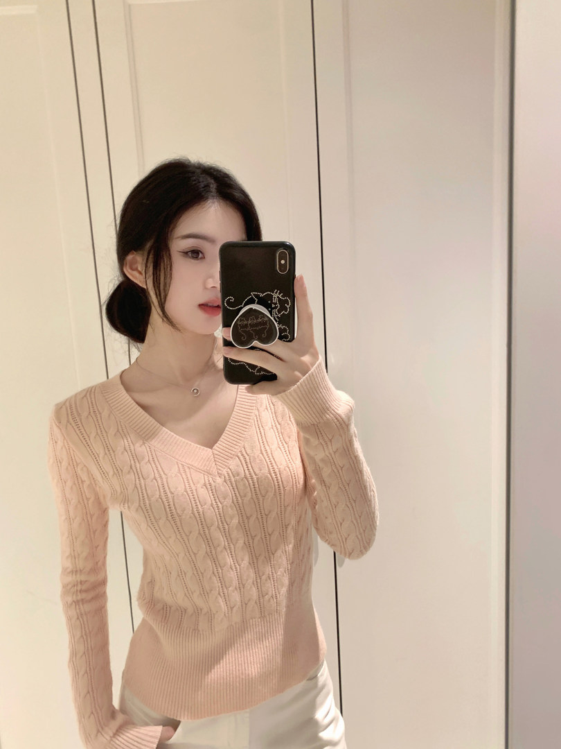 Woman taking mirror selfie wearing a light pink cable knit sweater