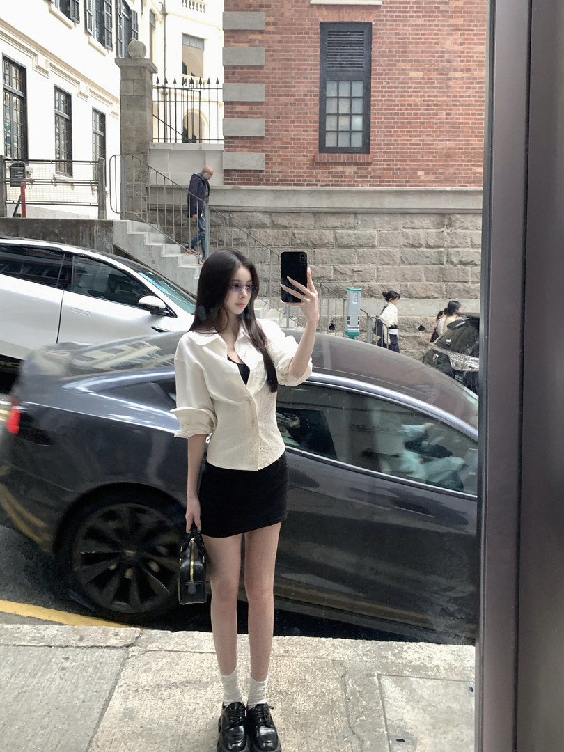 Woman taking a mirror selfie wearing a white blouse and black skirt with a handbag.