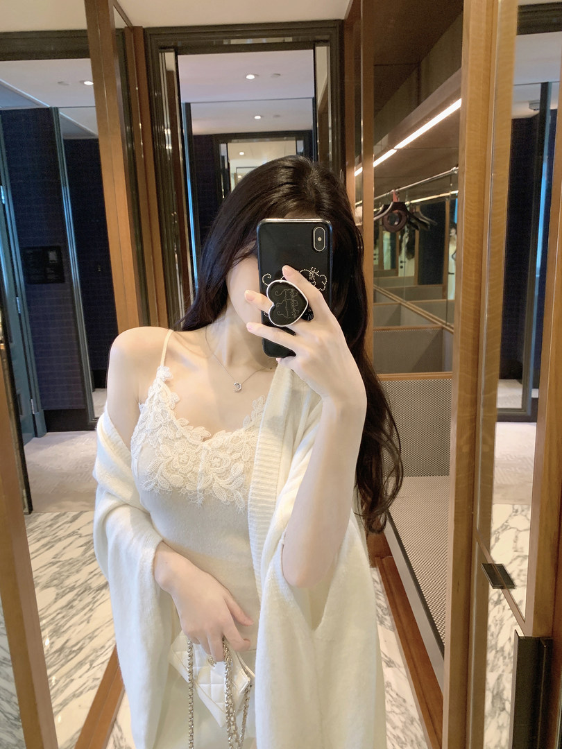 Woman taking mirror selfie wearing white lace camisole and cardigan