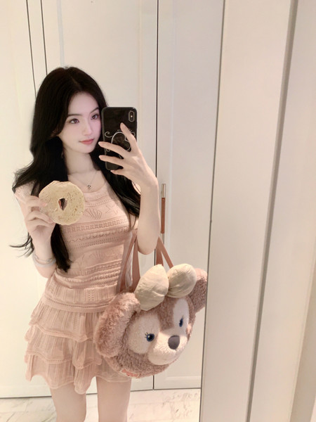 Woman taking mirror selfie wearing a peach lace dress and holding a donut, with a plush bear bag.
