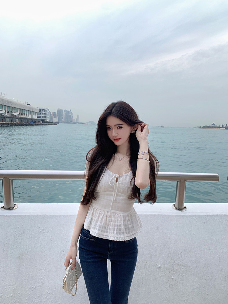 Woman wearing white lace-trimmed top and jeans by waterfront