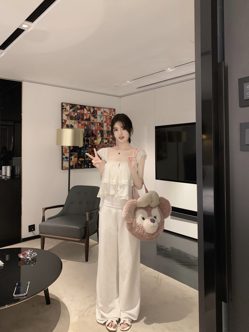 Woman wearing white ruffled top and wide-leg pants, holding a plush monkey bag.