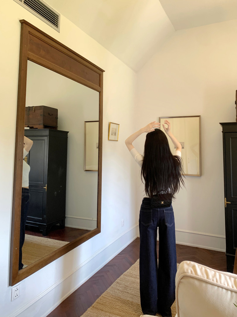 Woman wearing wide-leg jeans and a white top, standing in front of a mirror.