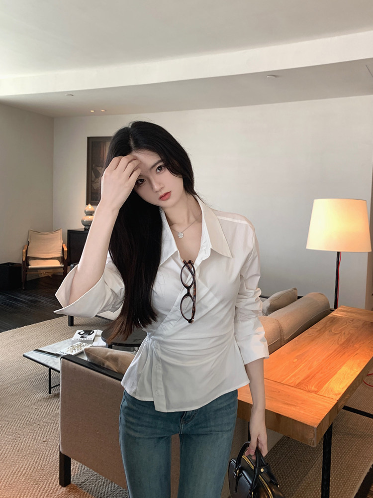 Woman wearing a white button-up shirt and jeans, holding a bag, in a modern interior setting