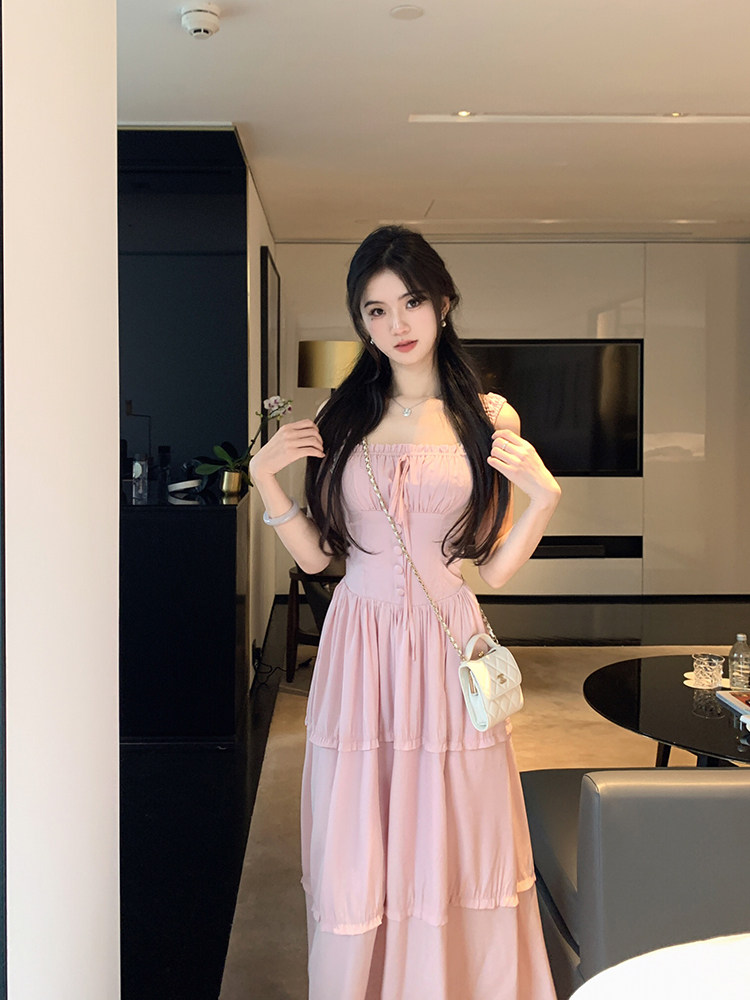 Woman wearing a pink tiered dress with a white handbag in a modern interior.
