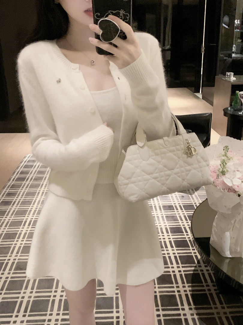 Woman wearing a white knit cardigan and matching skirt, holding a white quilted handbag.