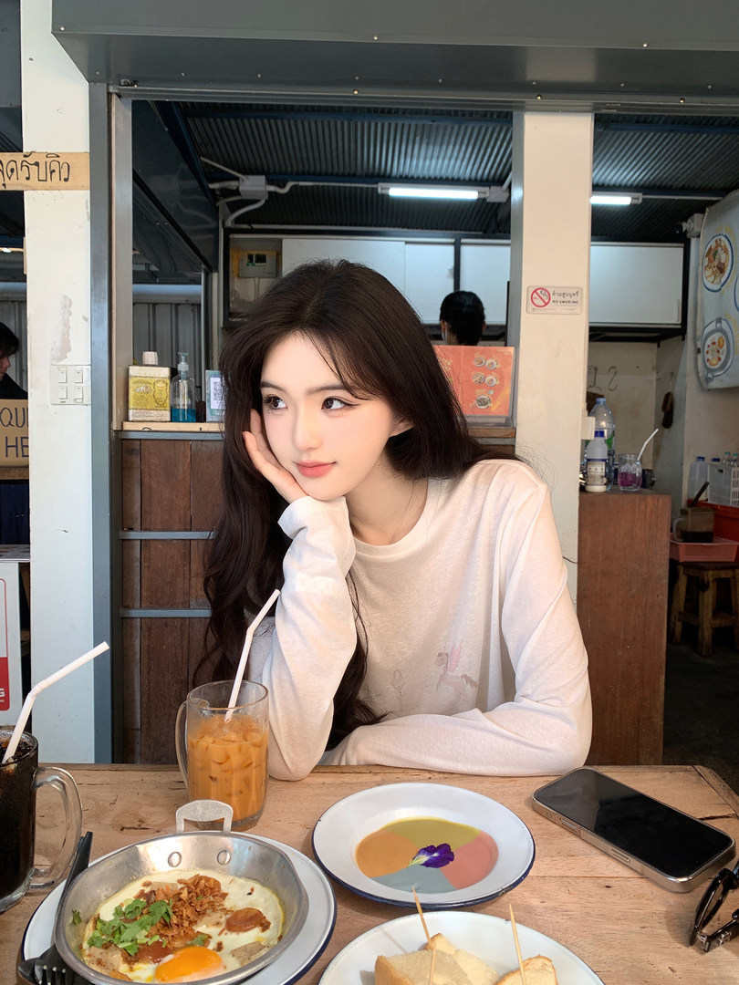 Woman wearing a white long-sleeve shirt sitting at a table with food and drinks