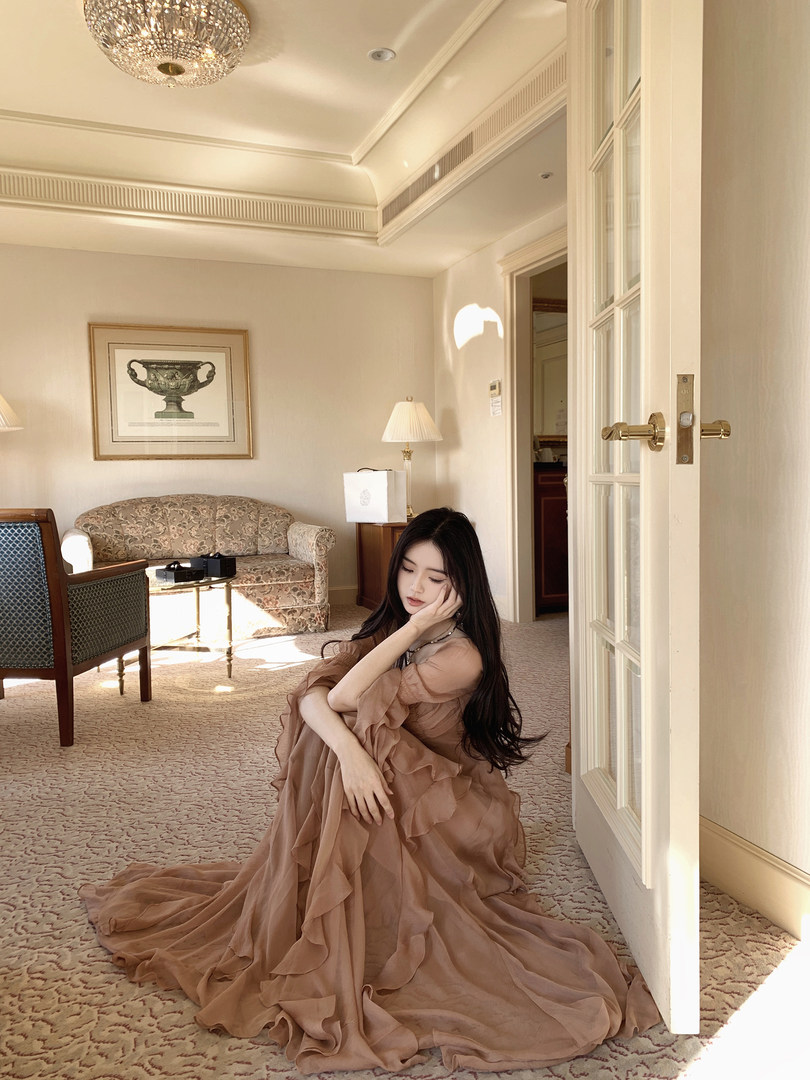 Woman wearing a long, ruffled, brown dress sitting on the floor in a luxurious room