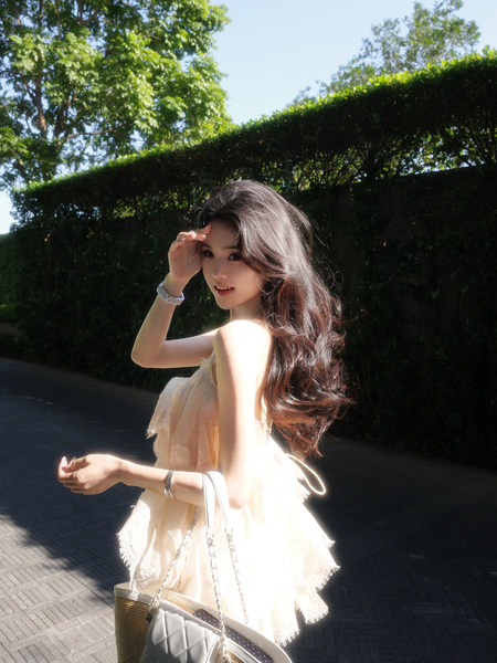 Woman wearing a light-colored lace dress outdoors with greenery background