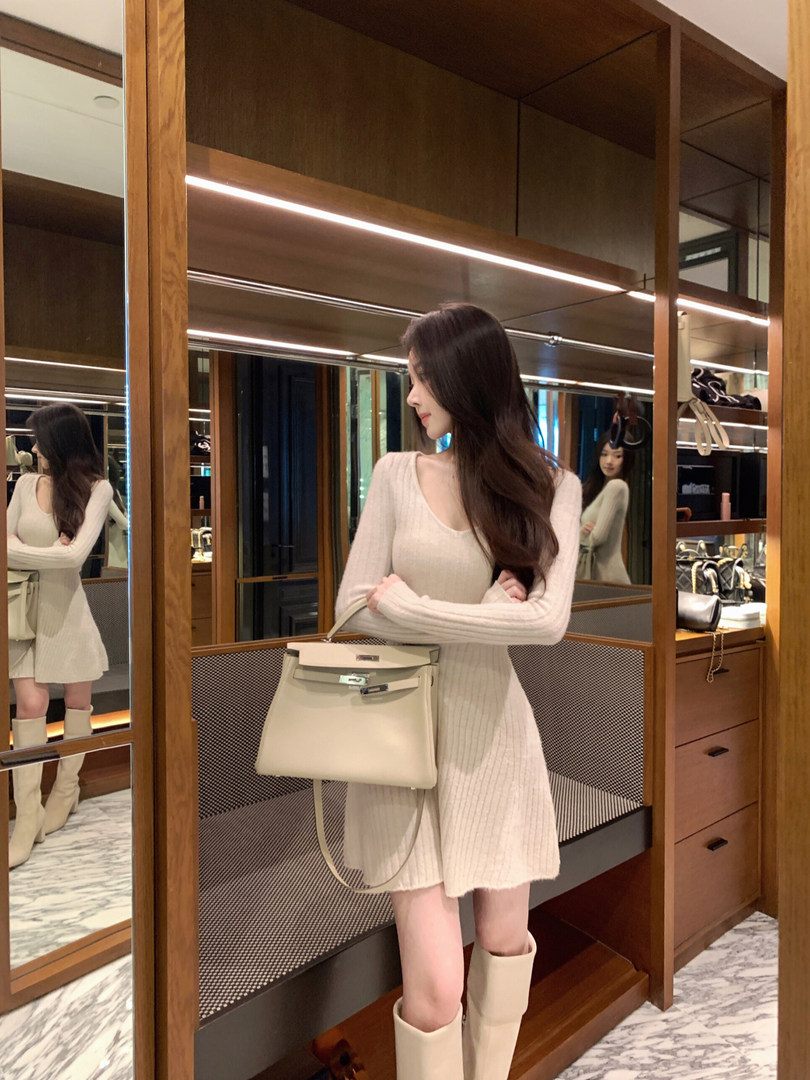 Woman wearing a cream ribbed knit dress with matching boots and holding a handbag, standing in front of mirrors.