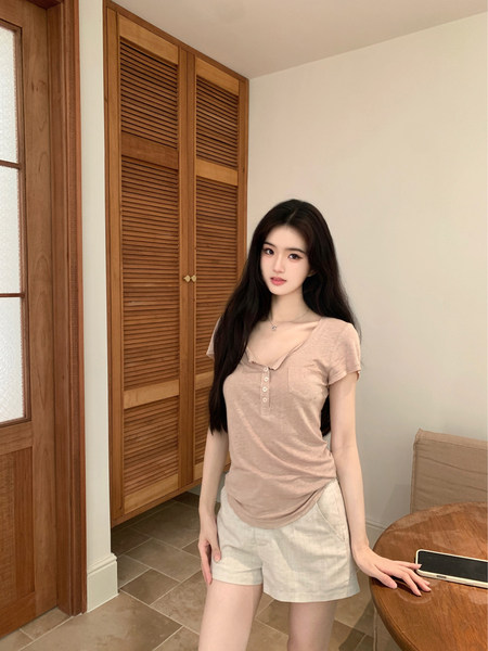 Woman wearing a beige short-sleeve top and light-colored shorts in a room.