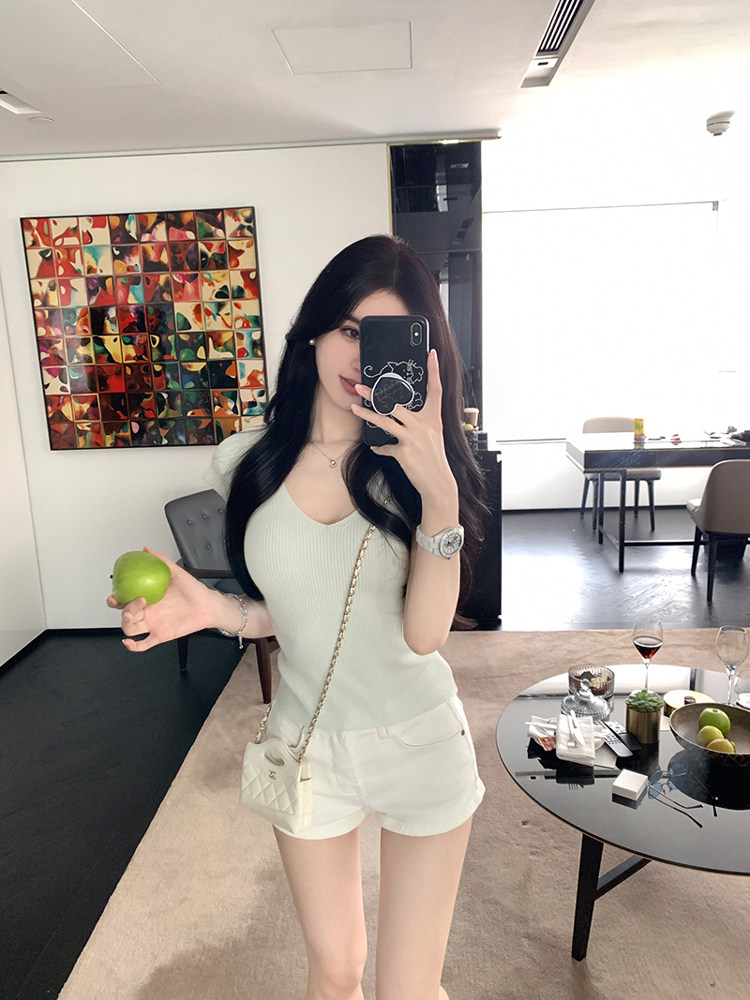 Woman taking mirror selfie wearing light green ribbed top and white shorts with small white handbag