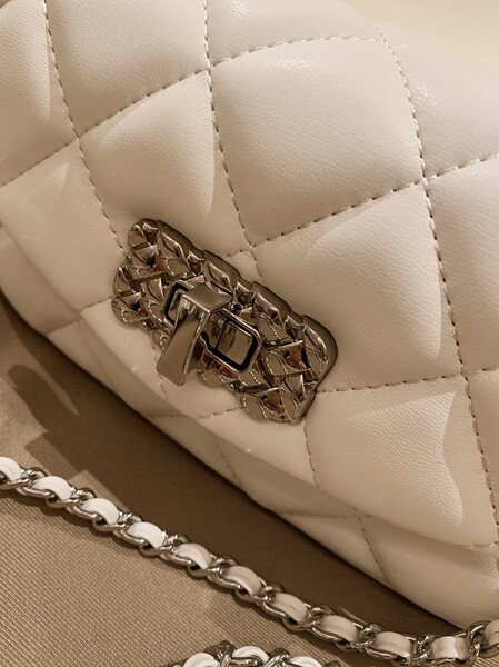 Close-up of a quilted white chain handbag with metallic clasp