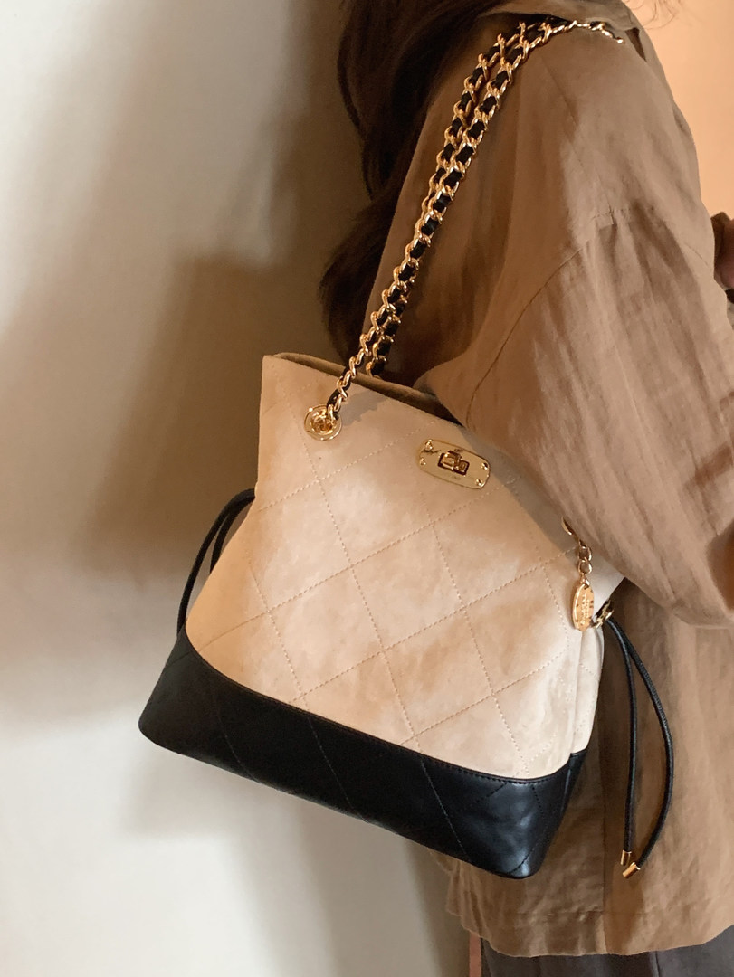 Quilted beige and black chain-strap handbag worn on shoulder
