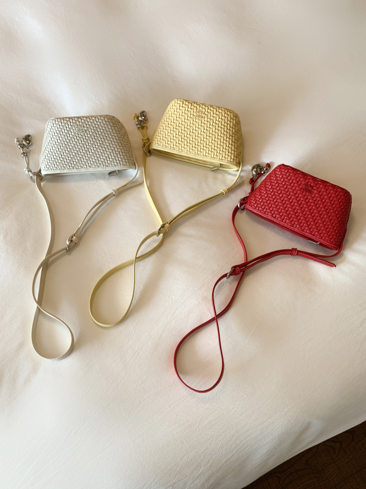 Three woven mini crossbody bags in white, yellow, and red on a light fabric background
