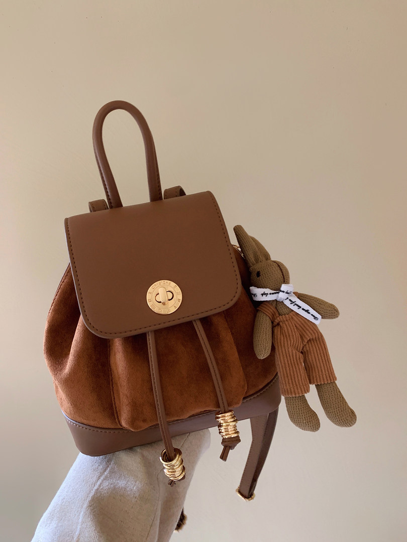 Brown leather backpack with a teddy bear charm shown on a person