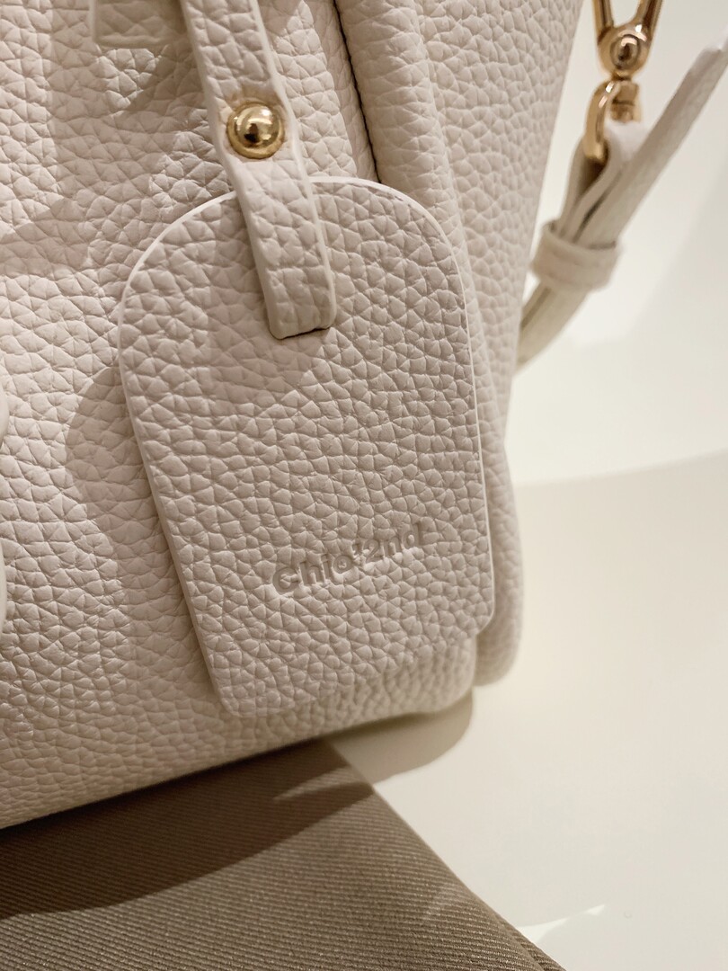 Close-up of a light beige textured leather handbag with gold hardware